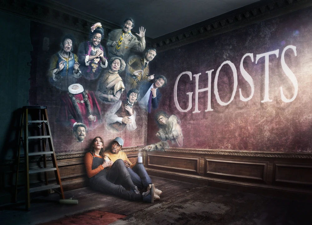 Several ghosts coming our of a wall above a couple sat on the floor with the wording Ghosts written across the wall