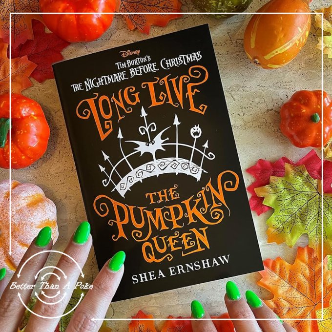 A festive table covered in small pumpkins with a pair of hands with green nail polish reaching for a copy of Long Live The Pumpkin Queen by Shea Ernshaw